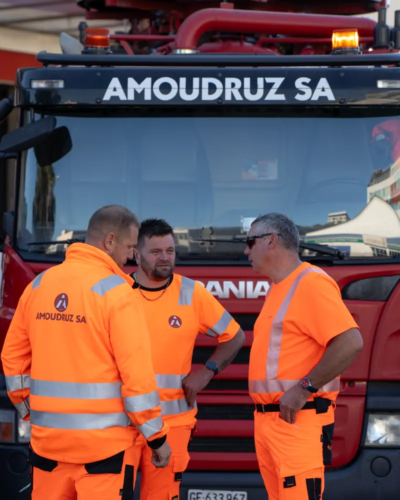 Trois collaborateurs d'Amoudruz SA échangent devant un camion de l'entreprise